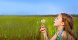 White girl in a field blowing a dandelion