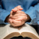 Folded hands in prayer on top of a Bible