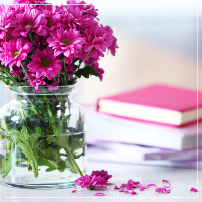 Pink flowers in a clear vase alone with books on a white table