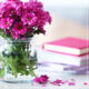 Pink flowers in a clear vase alone with books on a white table
