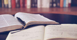 Open Bible, notebook, and pen on table in home library