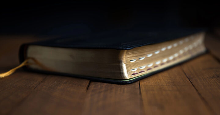 Black Bible with index tabs laying on dark wooden table