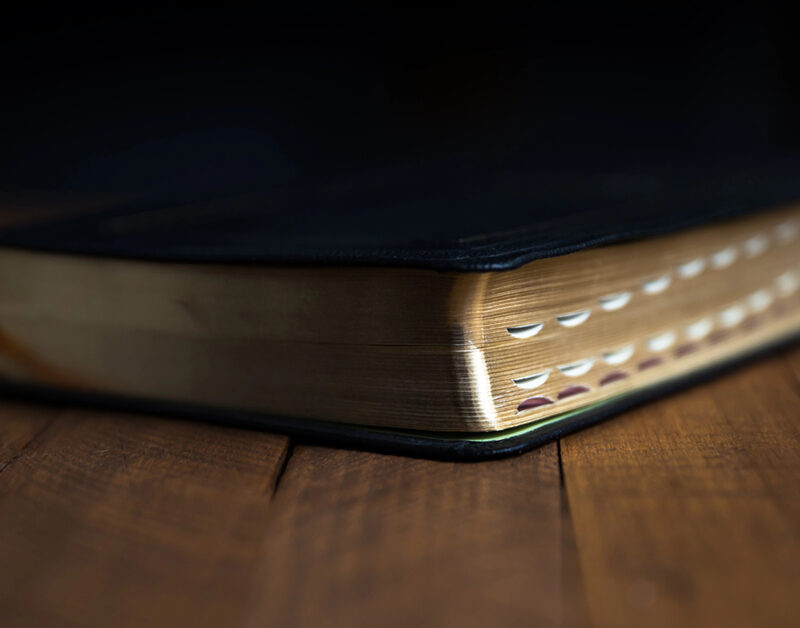 Black Bible with index tabs laying on dark wooden table