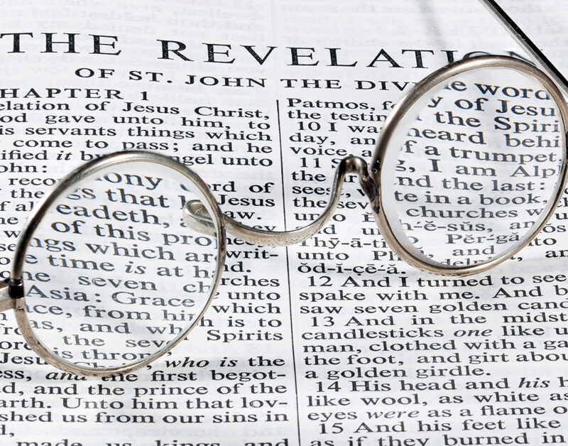The book of Revelation in the Bible with old-fashioned glasses laying on top