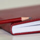 Red journal and red pencil on table