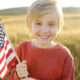 Cute blonde boy holding American flag in field