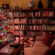 Christmas tree lit in dark room with wall of books