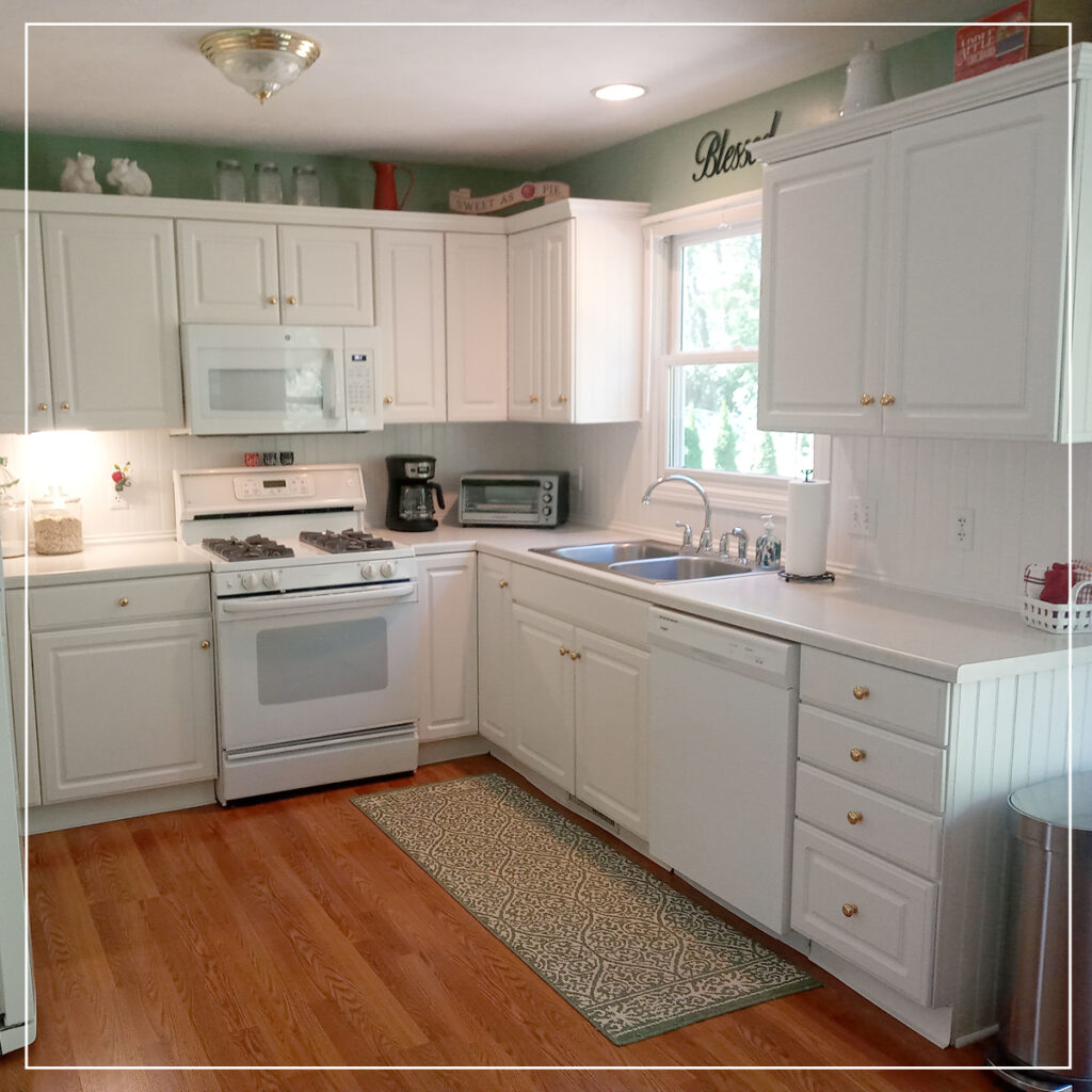 Kitchen with white cupboards, appliances, and warm oak wooden flooring