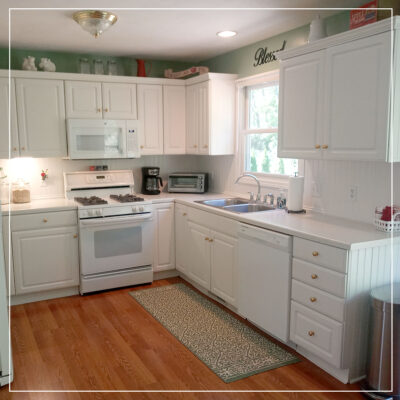 Kitchen with white cupboards, appliances, and warm oak wooden flooring