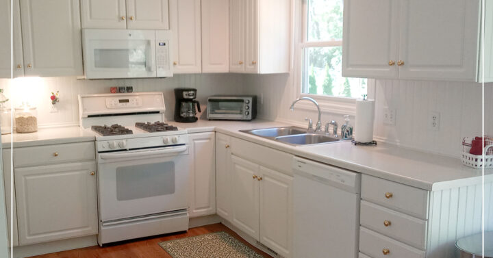 Kitchen with white cupboards, appliances, and warm oak wooden flooring