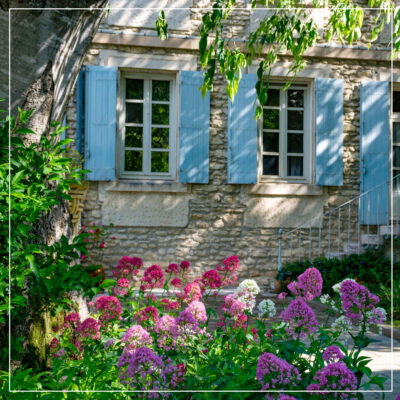 Stone house with light blue shutters and pink, red, and purple flowers in front
