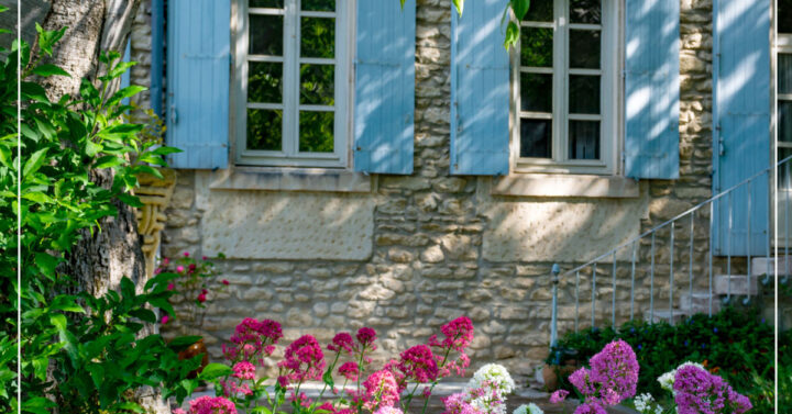 Stone house with light blue shutters and pink, red, and purple flowers in front