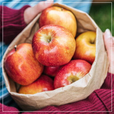 Woman holding brown bag of red apples