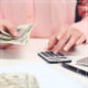 Women in pink sweater counting money and using calculator