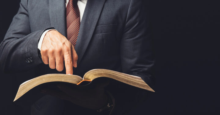 Man in suit and tie pointing to an open Bible