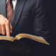 Man in suit and tie pointing to an open Bible